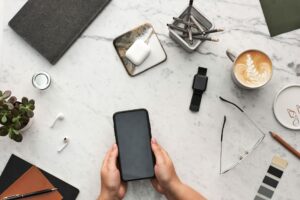 mesa com objetos e mão segurando celular com conta digital
